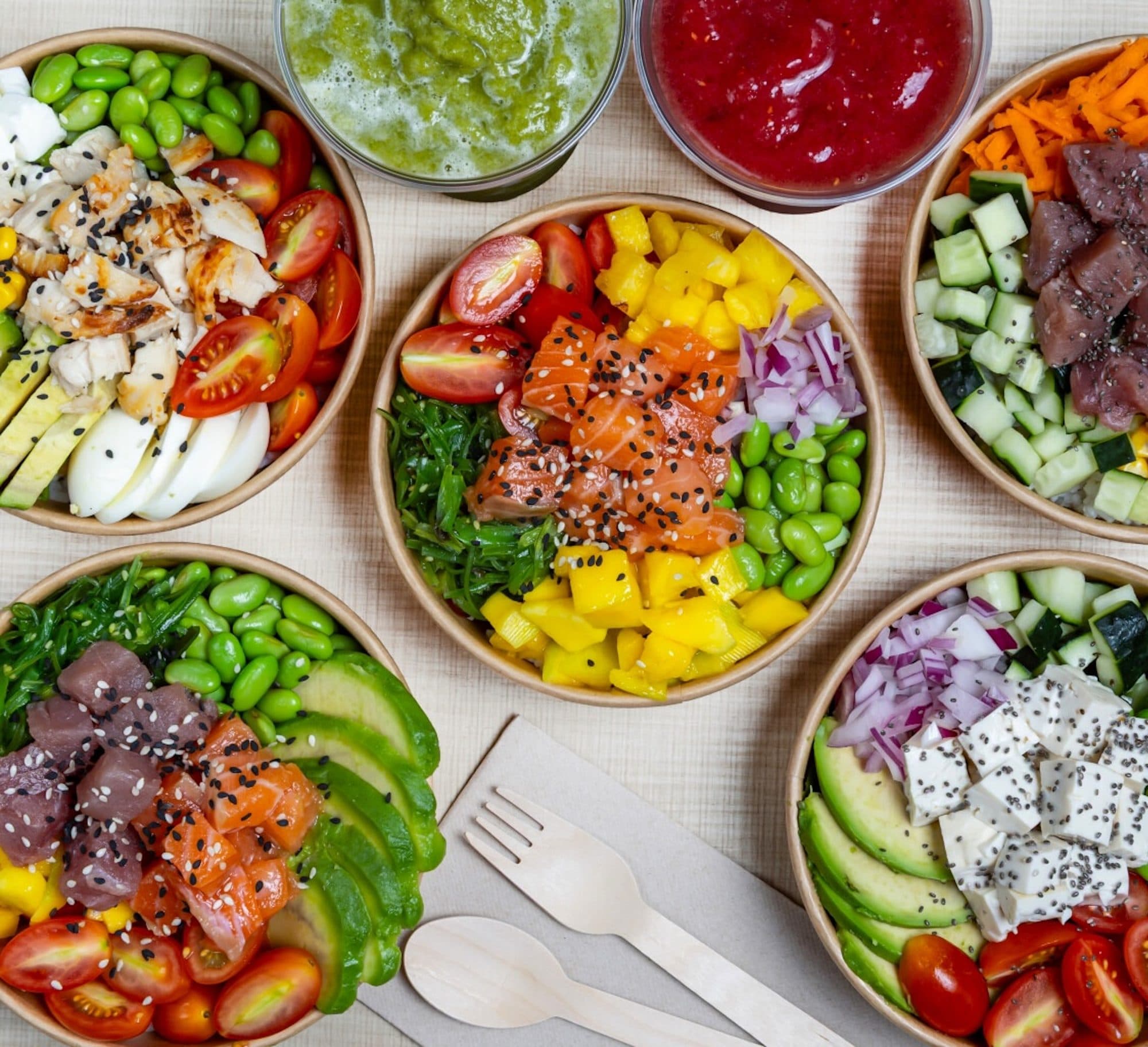Varios poke bowls de HŌKŌ Poke con salmón, atún, aguacate, edamame y mango vistos desde arriba